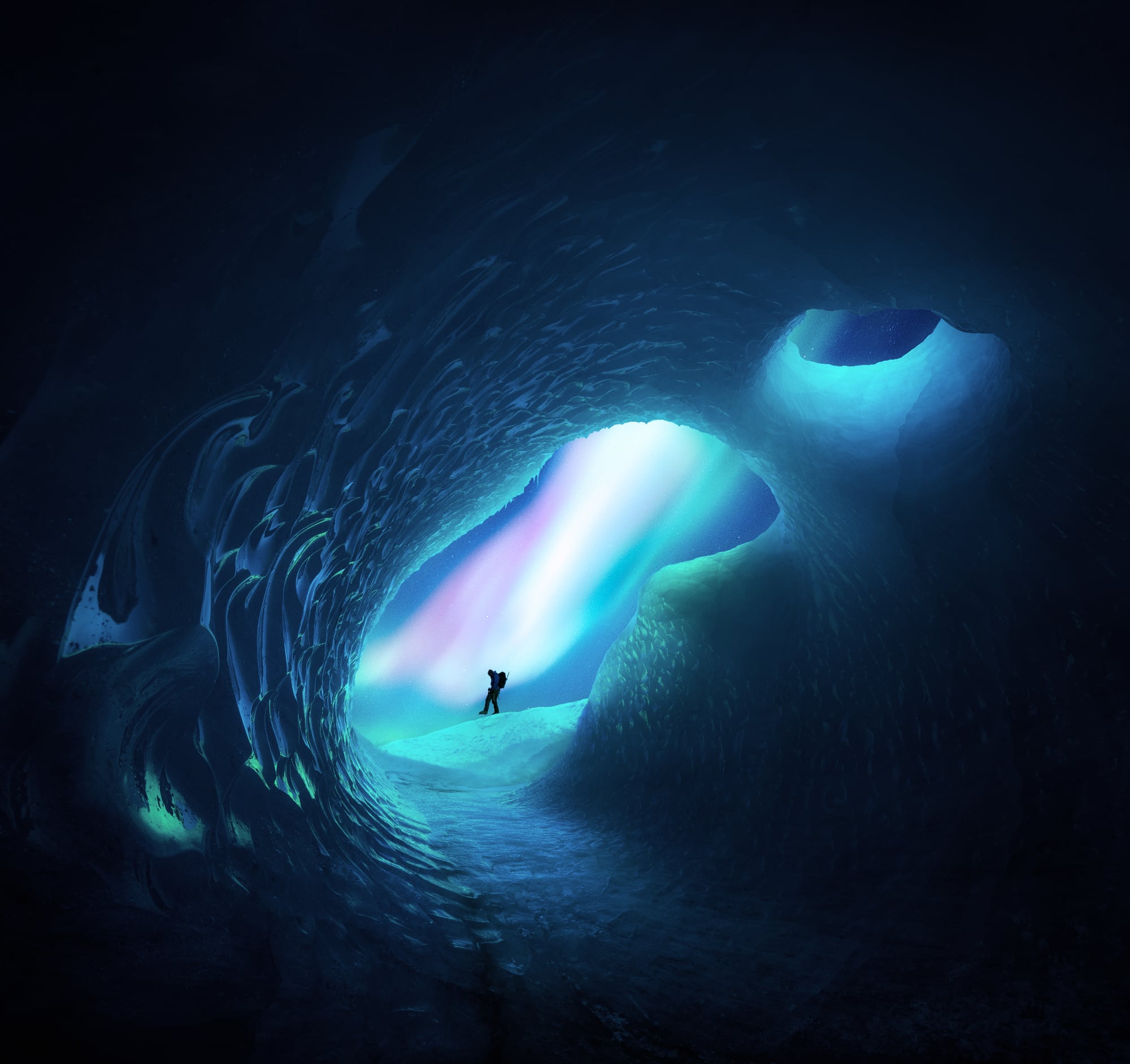 An explorer stands in the distance at the center of the opening of an ice cave with vibrant blue all around